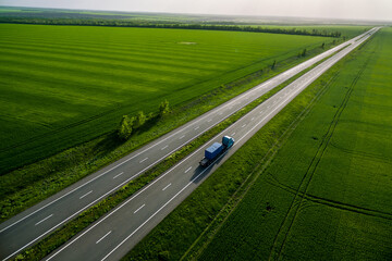 blue truck with container driving on asphalt road among the green fields. seen from the air. Aerial view landscape. drone photography.  cargo delivery