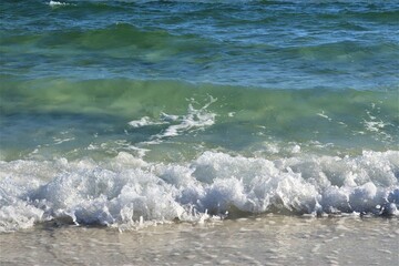 Waves from the ocean seethe and foam on the shore, forming white lambs and foam, close up