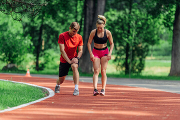 Obraz premium Young couple stretching before starting their morning jogging routine on a tartan track at the park.