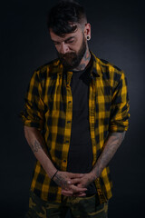 Attractive man with tattoos posing dressed in yellow and black checkered shirt on a black background