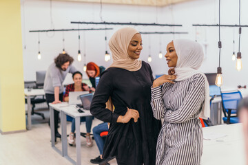 Obraz premium Portrait of two African American businesswomen talking to each other while standing in a modern business office with their colleagues. Marketing concept. Multi-ethnic society..