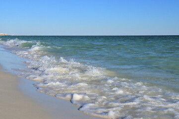 Waves from the ocean seethe and foam on the shore, forming white lambs and foam, close up