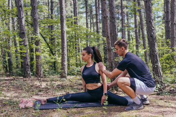 Young active couple doing stretching exercises in the woods on a yoga mat after jogging and running