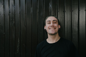 young man smiling in front of a dark wooden wall, happiness concept, man campaign, summer fashion