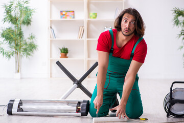 Young male contractor repairing heater indoors
