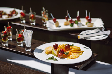 Appetizer at a wedding banquet, fruit pieces pineapple, pear, orange, strawberry, grapes decorated with mint leaves on a plate. Cutlery and buffet decoration.