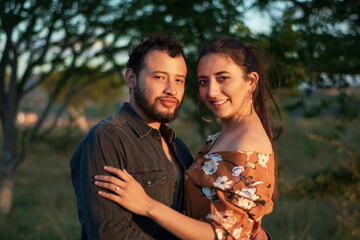 A romantic and lovely latin couple hugging each other in a beautiful sunny day with a dry grass field and a sunset in the background
