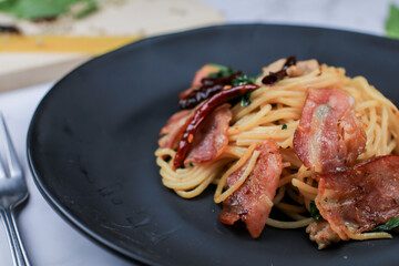 Spaghetti with dried chili and crispy bacon on black plate. Hot and spicy food, international cuisine