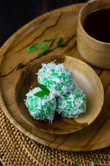 Klepon Rice Ball cake, Indonesian traditional sweet boiled cake, made from glutinous rice flour, pandan leaves, grated coconut, and palm sugar. Dark wooden background. Selective focus.  