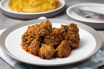 Ayam Kari or chicken curry, Indonesian traditional food served on ceramic plate, very popular at hari raya celebration food with roti canai, lontong, buras and ketupat. Grey wooden background.