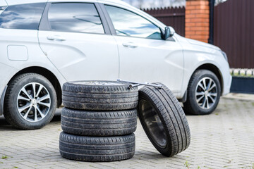 The wrench rests on the foot of the car wheels. An unknown white car on a blurred background. The concept of seasonal replacement of summer car tires with winter tires. Autumn day.
