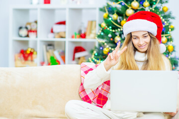 Young woman wearing Christmas hat, take video calls during coronavirus pandemic, with Christmas tree on the background. Coronavirus and Christmas concept. Holidays and Code of Conduct During Lockdown