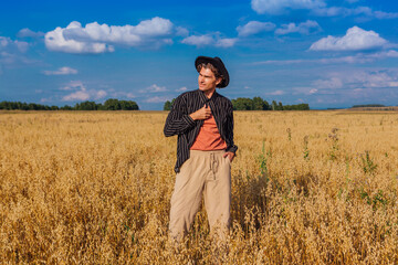 Naklejka na ściany i meble Tall handsome man with black hat standing at golden oat field.