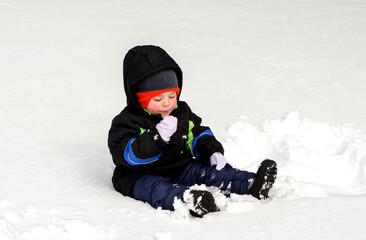 toddler boy in snow suit is happily  eating snow