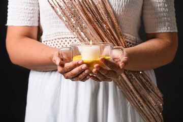 Woman holding burning candle for celebration of Divaly on dark background, closeup