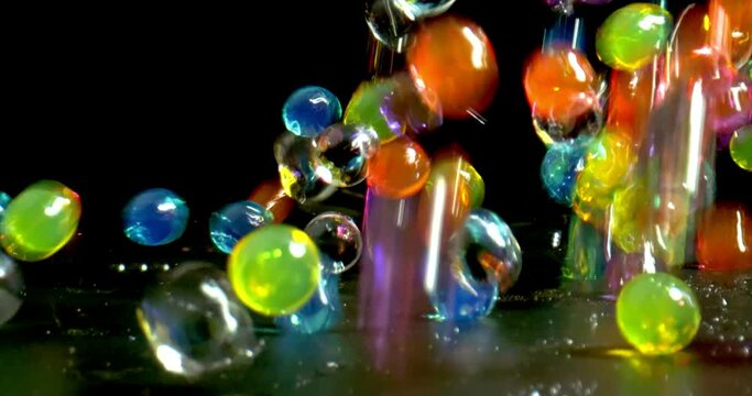 Colorful bouncing glossy wet balls with reflection close-up shot on black background. Wet balls jumping in slow motion and leaving water droplets on the background