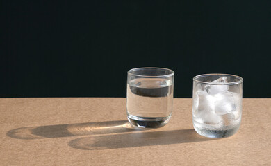 Glass of water and glass of ice cubes on table
