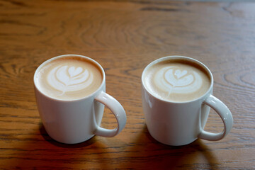Closeup twin Latte art fresh coffee in the white cup with white milk foam heart on top on the wooden table background. Drink or love and valentine concept.