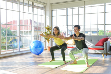 Young Asia couple practicing yoga lesson, breathing and meditating together in living room at home. healthy lifestyle concept