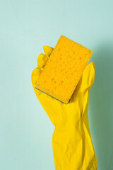 A hand in a rubber glove holds a foam sponge on a blue background.