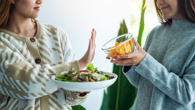 Women Choosing To Eat Vegetables Salad And Making Hand Sign To Refuse Potato Chips