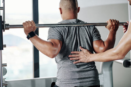 Fitness trainer asking client to keep back straight when doing squats with barbell