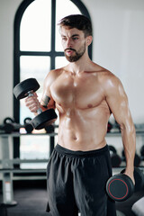 Fototapeta na wymiar Handsome strong muscular man lifting dumbbells when standing in gym