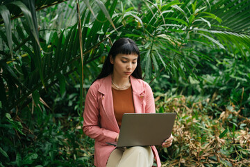 Asian woman in formal shirt sitting on a chair using computer laptop in nature.