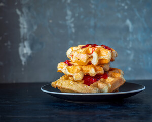 Stack of hard homemade waffles with raspberry jam on a gray plate