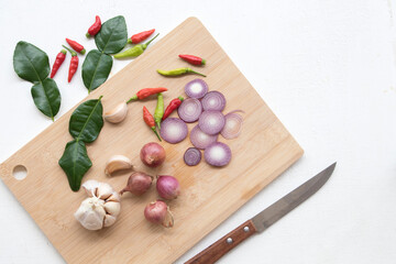 garlic ,lime ,red onion slice,lime leaf and pepper herbal vegetarian with knife on chopping block prepare to cook on tabla white