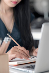 Cropped shot of woman hand writing on notebook with pencil while sitting at office desk.