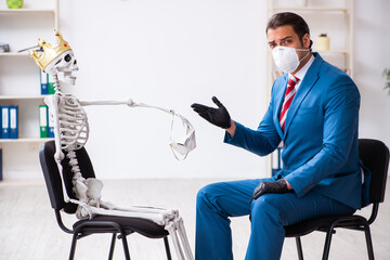 Young businessman and skeleton in the office in pandemic concept