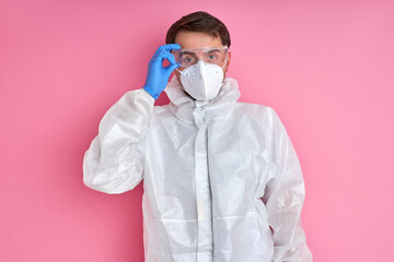 confident male doctor in protective suit is ready to prevent coronavirus, covid-19. he is posing, looking at camera isolated over pink background