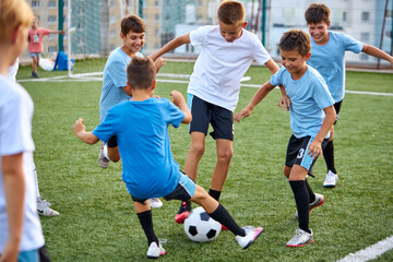 young caucasian school kids playing football in a field, stadium. boys 8-9 years old kicking soccer...