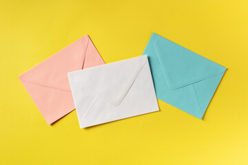Three envelopes of different colours, shot from above on a yellow background