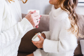 Mother and daughter in light sweaters are sitting on the sofa, the room is decorated for the new year and Christmas, hugs, conversations, smiles, kisses, waiting for a gift and magic