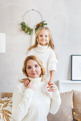 Mother and daughter in light sweaters are sitting on the sofa, the room is decorated for the new year and Christmas, hugs, conversations, smiles, kisses, waiting for a gift and magic