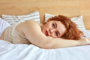 red haired chubby woman in lingerie lies on bed, have rest. sexy plus size model in white underwear enjoy, alone. body postive concept