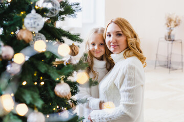 A girl with her mother near the Christmas tree, the interior decorated for the new year and Christmas, family and joy, traditions