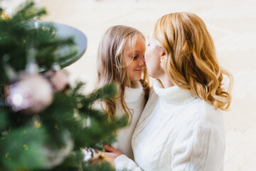 A girl with her mother near the Christmas tree, the interior decorated for the new year and Christmas, family and joy, traditions