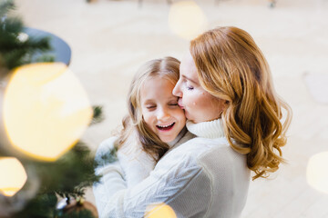 A girl with her mother near the Christmas tree, the interior decorated for the new year and Christmas, family and joy, traditions