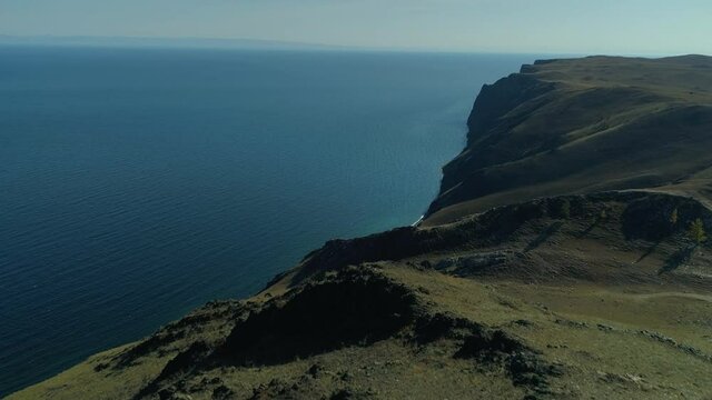 Aerial forward epic Baikal lake untouched autumn natural landscape. Hamar daban Seaside ridge high mountains. Blue beautiful water. Open space horizon. National park reserve Russia. Sunny day blue sky