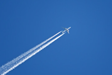 An airliner flies high in the blue sky leaving a white contrail behind it