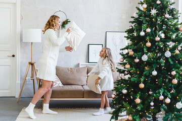 Girl and mother fight with pillows, games and entertainment before the new year and Christmas, the house is decorated with a Christmas tree and decor