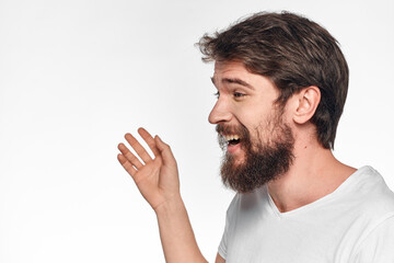 cheerful bearded man in a white t-shirt emotions gestures with his hands light background studio