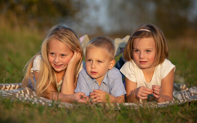 Sisters and little brother lie on the grass. Children play in the meadow. A happy family.