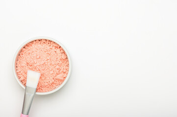 Pink alginate mask powder in bowl with brush on white background top view. Cleansing lifting face mask with collagen and acids. Clay texture, dry powder. Cosmetic cleansing beauty skincare product
