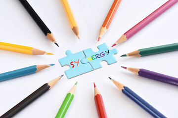 Synergy word on blue puzzle with colored pencils isolated on white background. Business team...