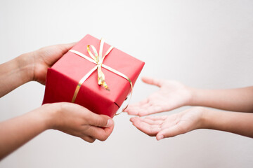 Closeup photography of hands holding a red box gift and little hands receiving on white background.