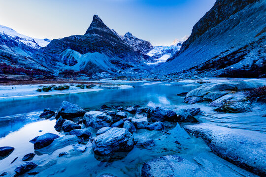 A river flowing through a valley in late autumn with snow capped mountains in the background and rocks in the foreground
